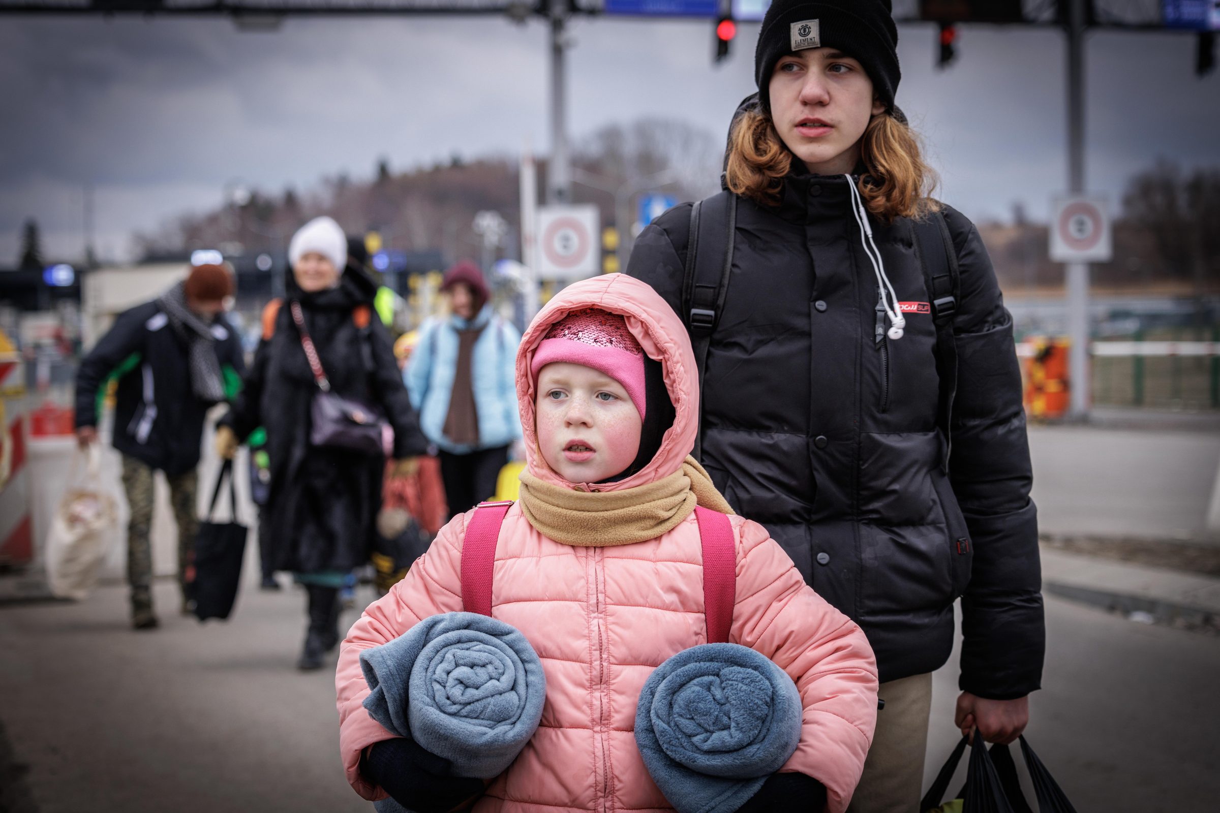 Girl in pink coat with rolled blankets at the crossing